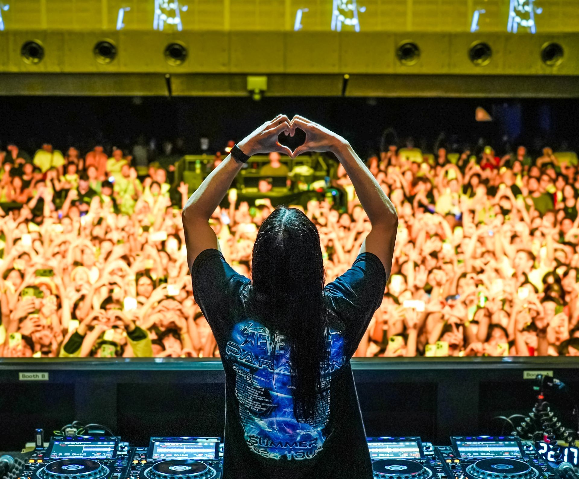 DJ on stage making heart shape with hands toward enthusiastic audience in a concert setting.